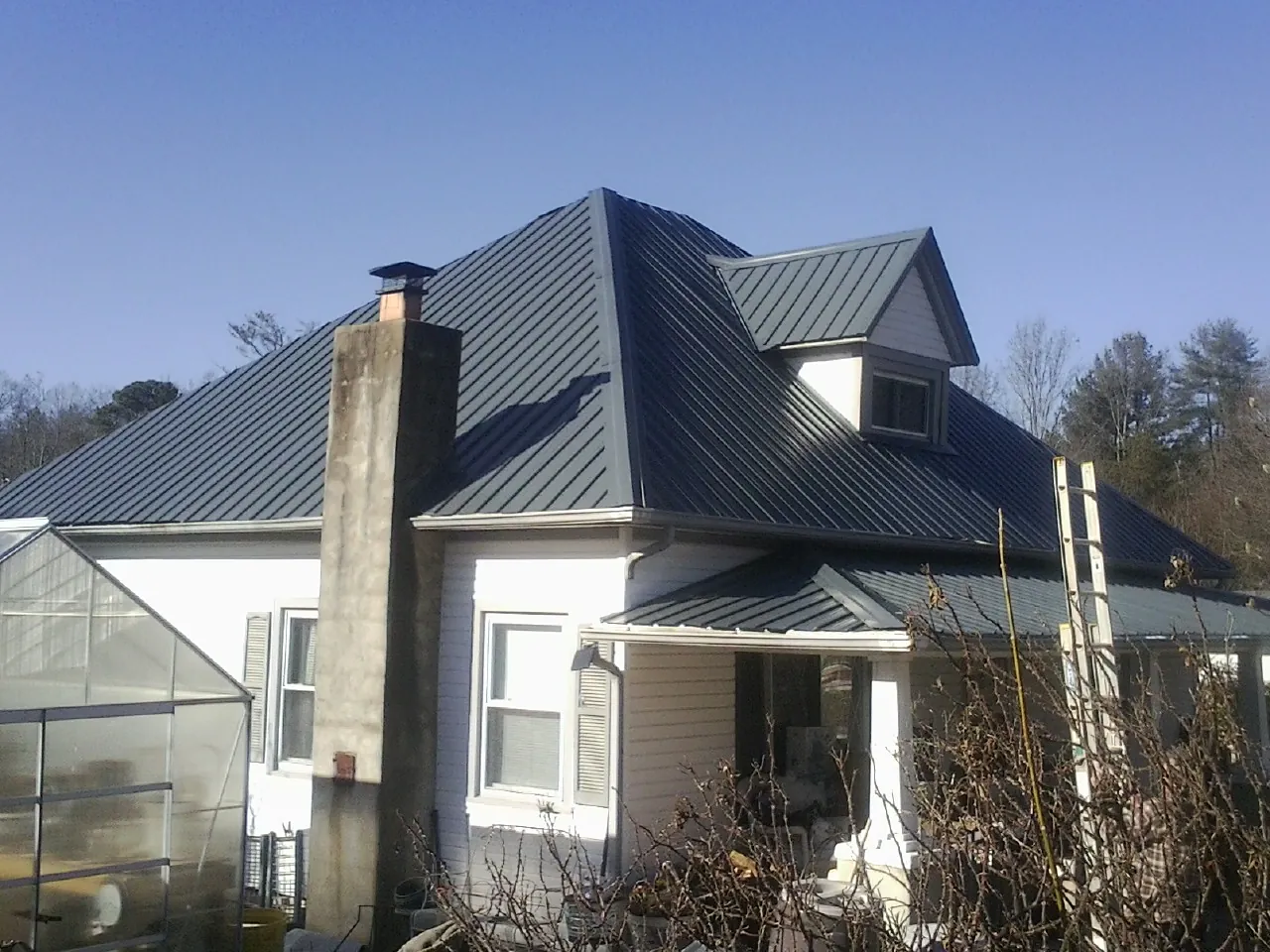 Dark blue standing seam metal roof on a white farmhouse with dormer — Slate & Tile Roof Repair by Roofing Brothers in Lehigh