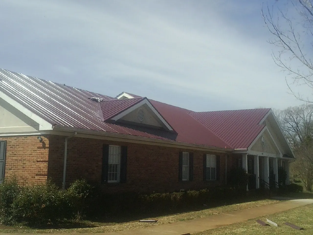 Red metal roof with gabled entries on a long brick building, from a Hail Damage Roof Repair job in Lehigh