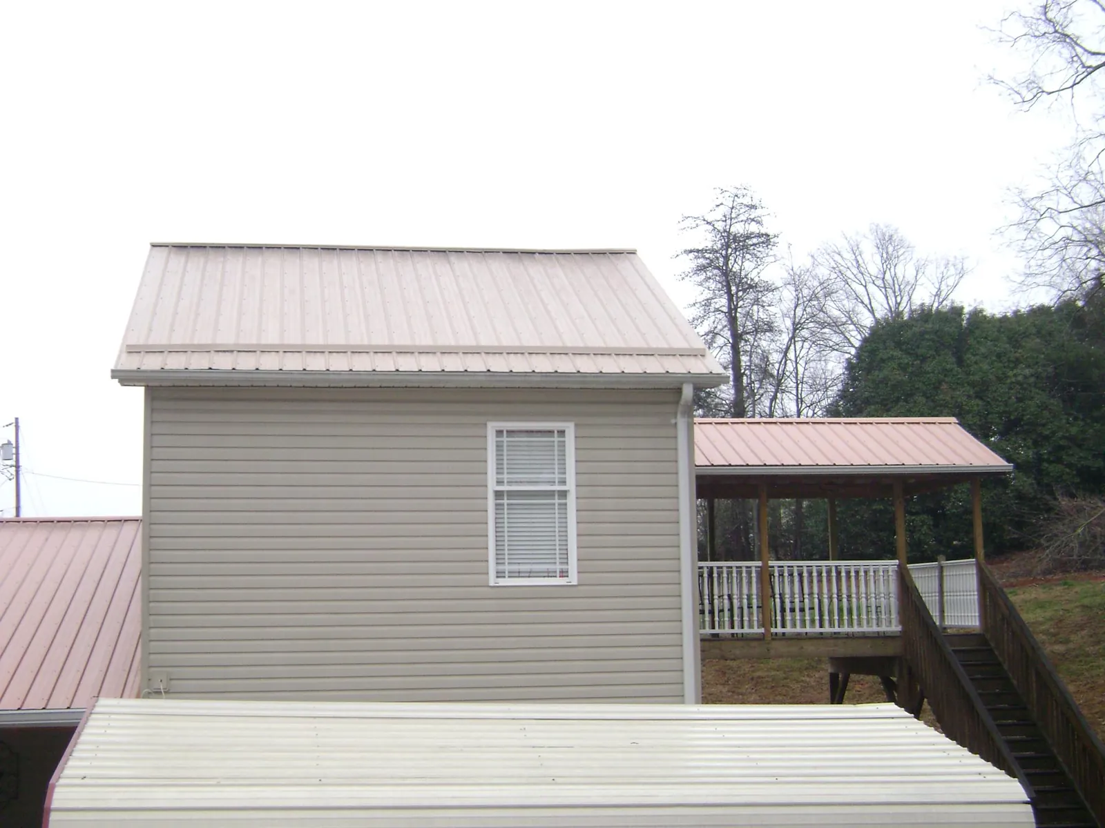 Tan metal roofs on a two story addition and attached porch, from a Roof Replacement job in Lehigh